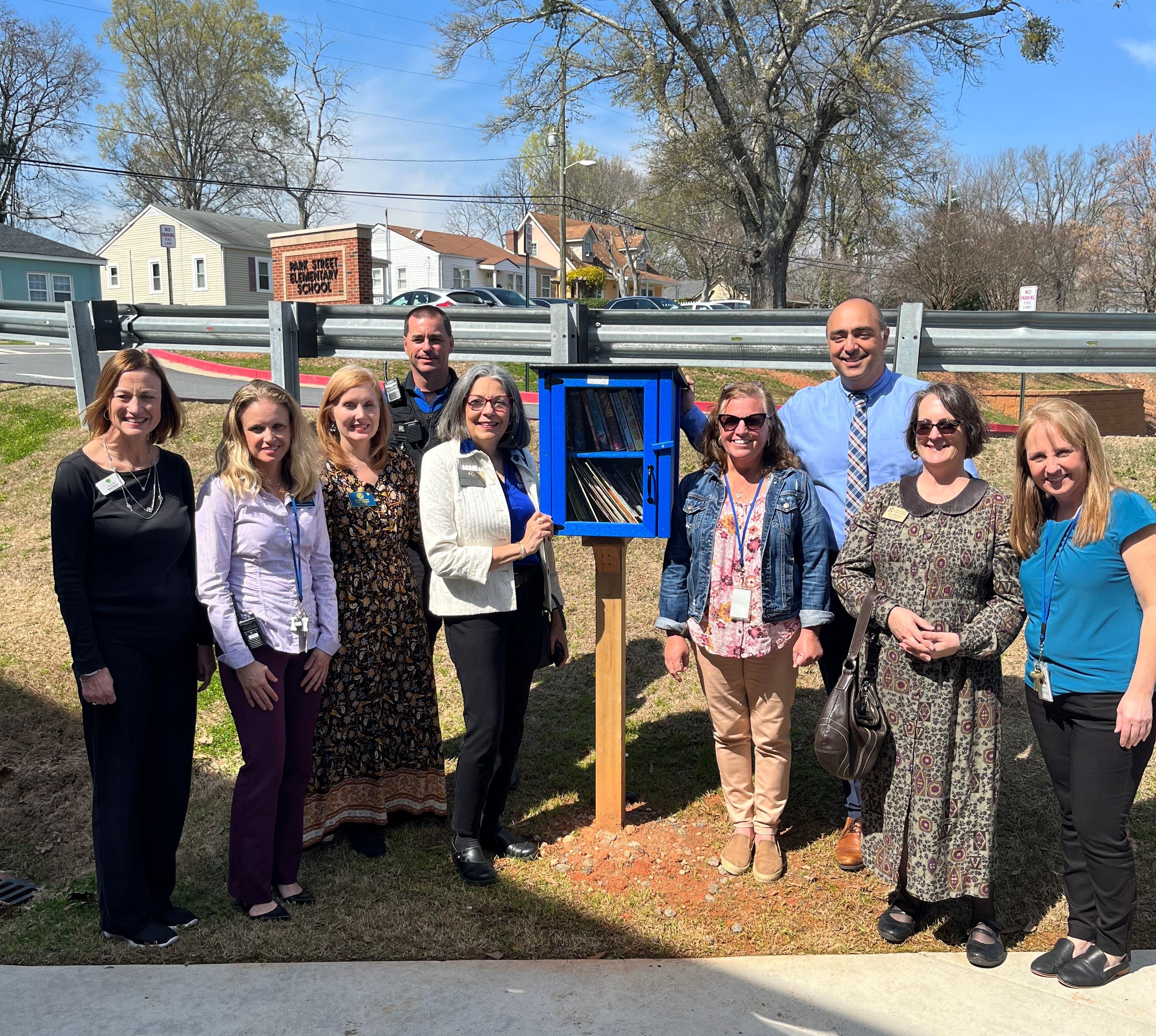 Smiling adults standing around a Free Little library outsides